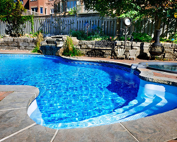 Residential inground swimming pool in backyard with waterfall and hot tub